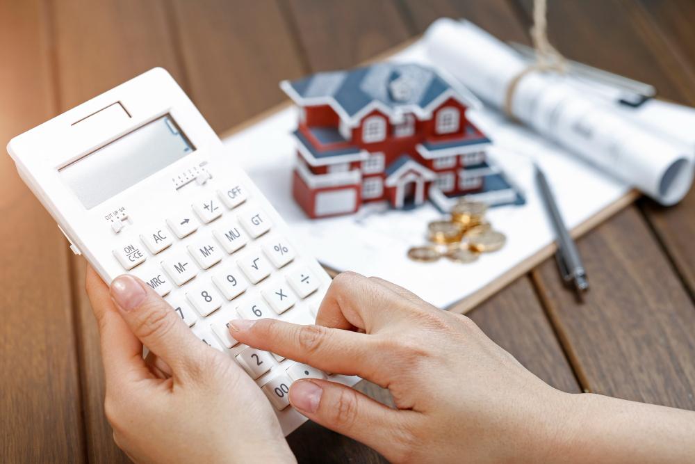 une main féminine exploitant une calculatrice devant un modèle de maison de villa